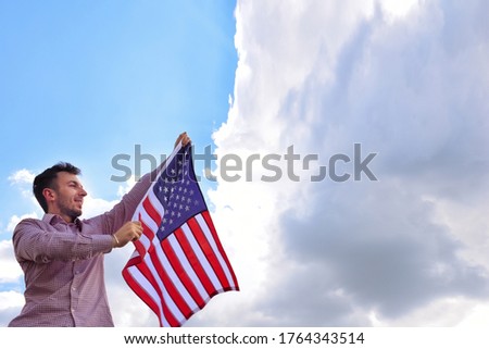 Happy young man with American flag on a nice summer day, symbol of Independence Day, July 4th, against background of dramatic blue sky