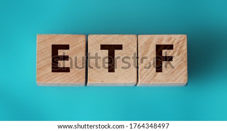 ETF, Exchange Traded Fund, realtime mutual index fund that can trade in equity stock market, cube wooden block with alphabet building the word ETF on aquamarine blue paper.