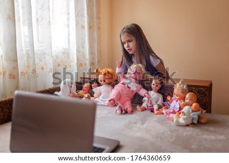 New normal life. Cute girl playing with dolls together with her friends via video chat, stay safe, social distance after lockdown, new happy childhood