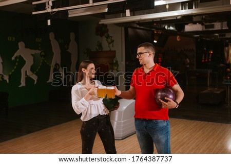 A caucasian woman and a man at the bowling alley with mugs of beer. Love and bowling