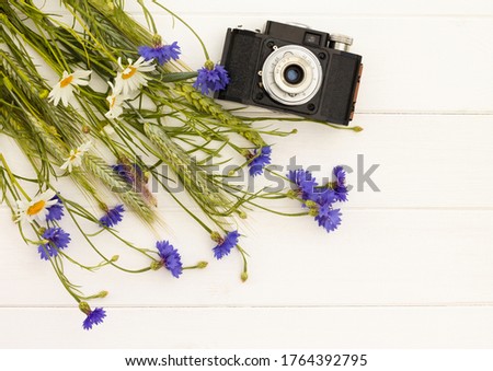 Retro vintage old camera with cornflowers and daisies on white wooden background. Top view. Copy space.