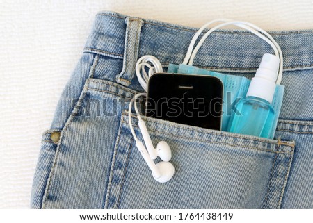 Medical face mask ,hand sanitizer spray and smart phone in jeans back pocket background. Concept for the new normal or new lifestyle after COVID-19 Coronavirus pandemic. 