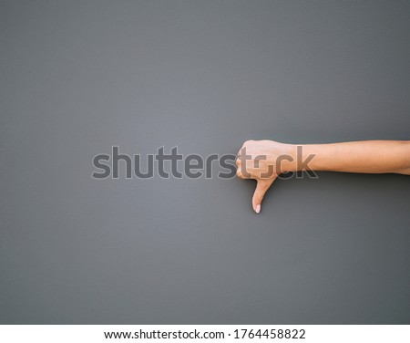 Women's right hand showing thumb down dislike isolated on gray background.