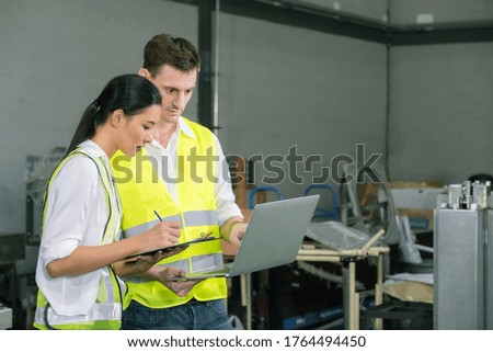 Male and Female Industrial Engineers in Hard Hats Discuss New Project while Using Laptop. They Make Showing Gestures.They Work in Industry Manufacturing Factory.