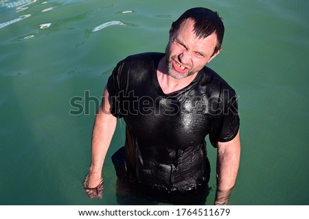 A top photo of a wet man standing in water in a black T-shirt