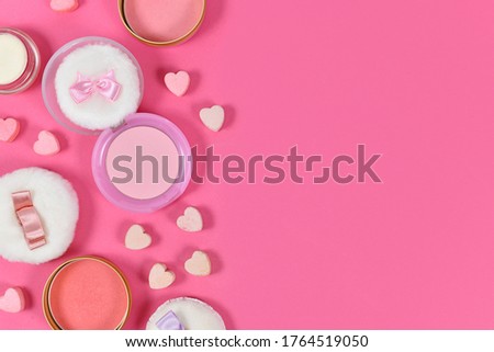 Various pink blush beauty products and powder puffs with ribbons and heart shaped pressed powder on pink background with copy space