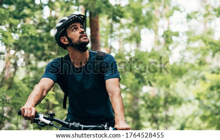 Outdoor image of handsome cyclist man riding bike in the mountain. Male athlete in cycling gear practising outside in the forest on nature background. Travel and extreme sport concept.