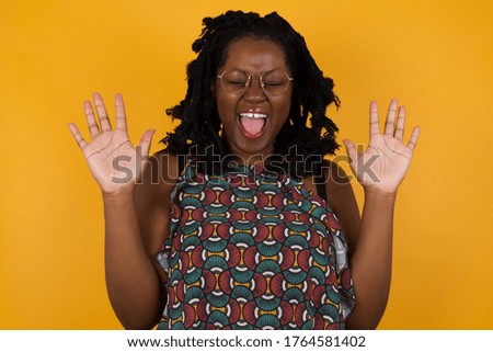Emotive eYoung afro american woman wearing glasses over isolated yellow background laughs loudly, hears funny joke or story, raises palms with satisfaction, being overjoyed, amused by friend. 