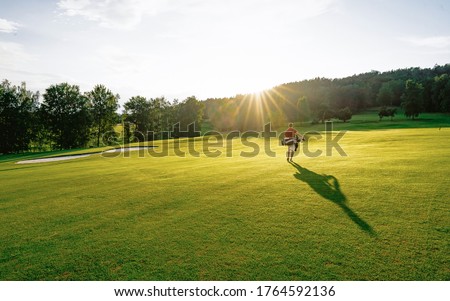 Golf player walking and bag on course during summer golf game in soft focus at sunlight. Sport playground for golf club concept - wide landscape as background for your lettering about golf playing. Royalty-Free Stock Photo #1764592136