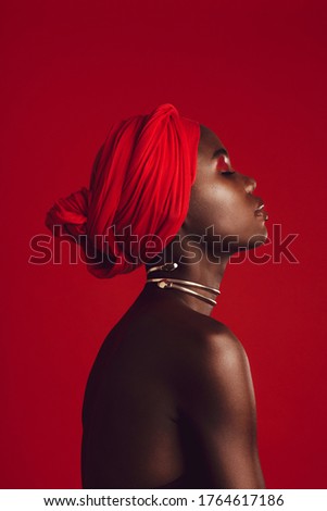 Side view of a woman with red turban in studio. Stylish female model with her eyes closed against red background. Royalty-Free Stock Photo #1764617186