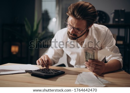 Serious man checking bills and counting money at office Royalty-Free Stock Photo #1764642470