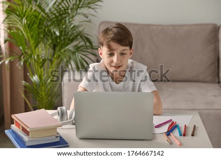 A focused boy sits on the couch and does homework at the table.