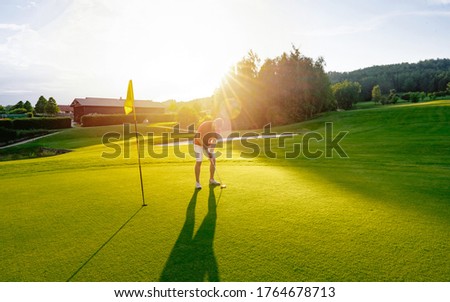 Golf player putting golf ball to hole during sunset or sunrise. View of Golf Course with beautiful green field. Golf course with a rich green turf beautiful scenery. Sport concept 