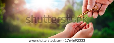 Hand Of Father Giving Old Golden Key To Child In Garden - Death And Inheritance Concept Royalty-Free Stock Photo #1764692333