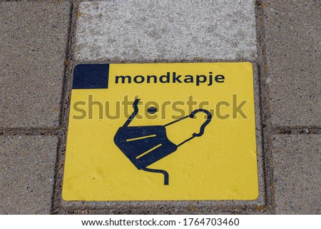 Caution sign board on the floor, Yellow and black tape on the railway platform with a Dutch word "mondkapje" "face mask" Reminding travelers that face mask is compulsory in all public transportation.