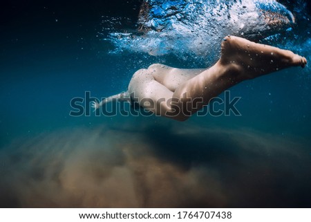 Woman dive without surfboard under ocean wave. Underwater duck dive under wave and sandy bottom
