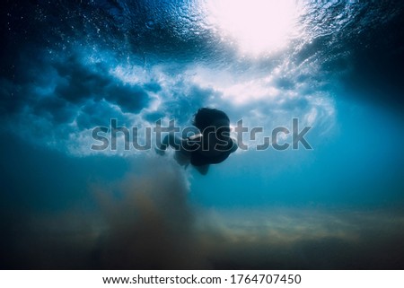 Woman dive without surfboard under ocean wave. Underwater duck dive under wave and sandy bottom