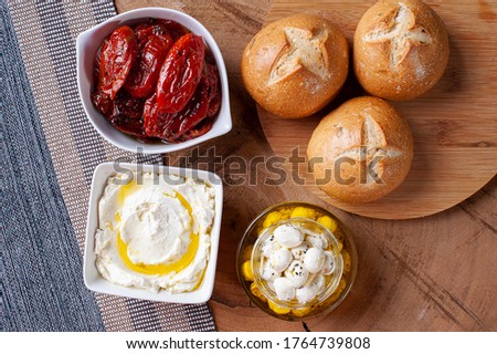Wooden table with 2 types of curds and sun-dried tomatoes to accompany bread.