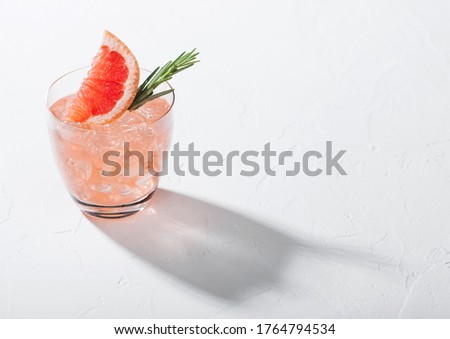 Glass of refreshing summer red grapefruit cocktail with ice cubes, fruit slice and rosemary on white background. Space for text