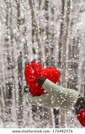 Woman hand holding a red heart on a snowy background
