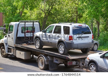 A white van chained to a modern flatbed tow truck. There is also a vehicle being towed.   Royalty-Free Stock Photo #1764844514