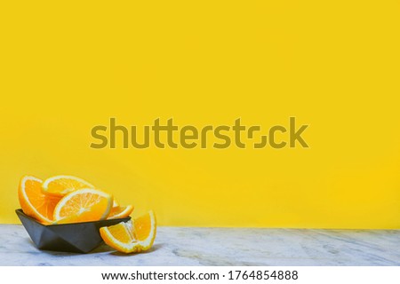 Sliced oranges in a black late on yellow background. Copy space