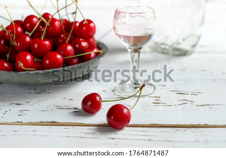 Strong alcoholic cherry drink Kirsch or Kirschwasser -  in a glass and fresh cherry on the white wooden table