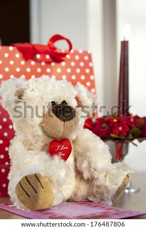 Teddy bear and gift bag with greeting card and red candle on background. Birthday or Valentine's day presents.
