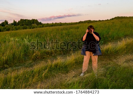 Picturesque summer landscape. In the foreground, a woman takes photos with a camera, in the background, a hilly terrain with high grass.
