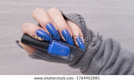 Woman beautiful hand with long nails and blue manicure with bottles of nail polish