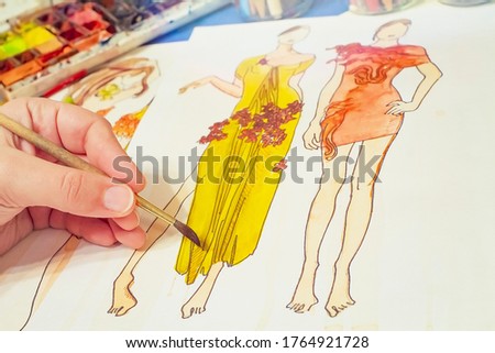 Fashion designer at work. He comes up with a new dress for the girl. Drawing with watercolors on paper in the process.
