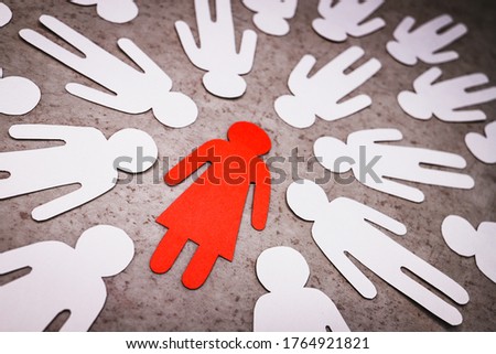 A red paper figure of a girl stands on a gray background. White silhouettes of men are directed at her. Symbol of sexism in the male collective. Aggression and disrespect for a woman. Royalty-Free Stock Photo #1764921821