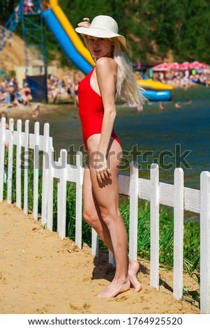 Portrait of a young beautiful girl in a solid red swimsuit posing on the beach