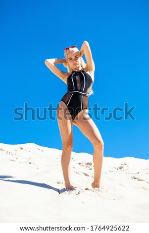 Portrait of a young beautiful blonde girl in black swimsuit on a background of blue sky