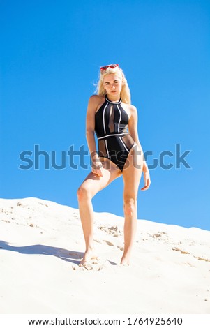 Portrait of a young beautiful blonde girl in black swimsuit on a background of blue sky