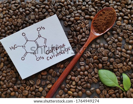 Structural chemical formula of caffeine molecule with roasted coffee beans and wooden spoon filled with coffee powder. Caffeine is a central nervous system stimulant, psychoactive drug molecule. Royalty-Free Stock Photo #1764949274