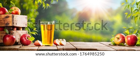 Apple Crate And Glass Of Juice On Wooden Table With Sunny Orchard Background - Autumn / Harvest Concept Royalty-Free Stock Photo #1764985250