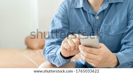 Business & Technology lifestyles background concept.Close up young Asian man wear blue shite holding smart phone for using online website  sit on sofa living room at home office.copy space. 