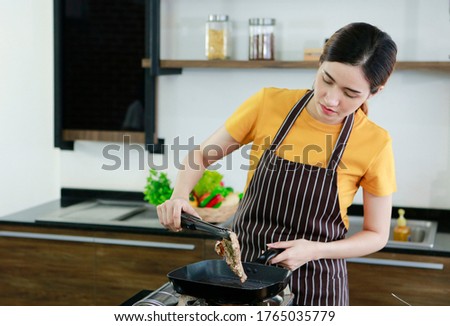 Asian women present fresh food. Shot housewife trying to cooking and showing pork steak in kitchen in house to take picture for sell food box online. Work from home / Stay at home / covid19 concept 