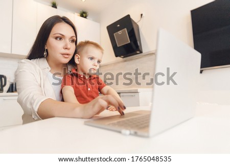 Business mom is using laptop, woman spending time with her boy baby home.