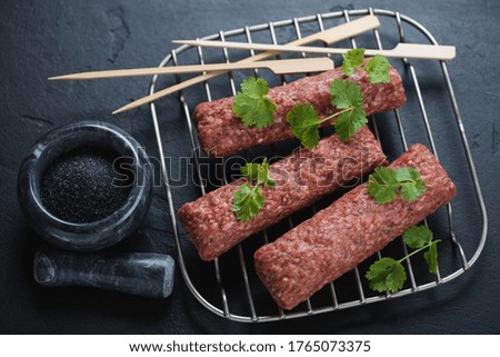 Metal rack with raw fresh kebabs made of marbled beef meat, studio shot over black stone background