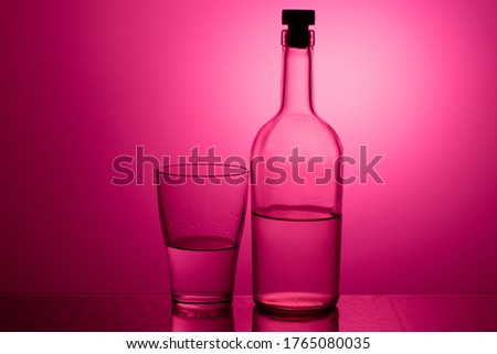 bottle of alcohol with a stopper and a glass on a purple background. glass on gradient background