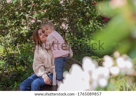 Happy daughter embracing her mother while relaxing together on park bench.