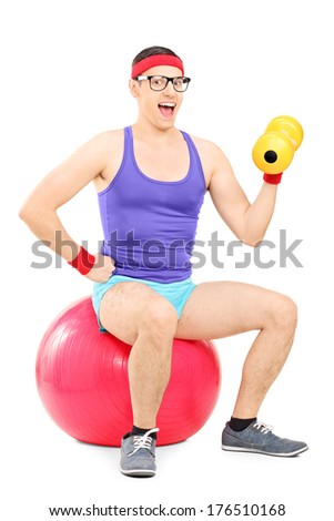 Nerdy guy sitting on pilates ball and lifting a dumbbell isolated on white background