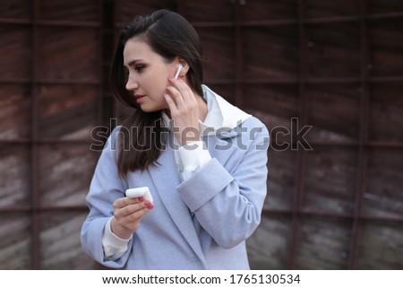 Portrait of a beautiful young girl in a blue coat with wireless headphones