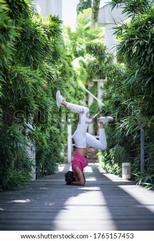 Beautiful young fitness girl doing yoga poses on the ground in a pathway surrounded by plants in a greenhouse