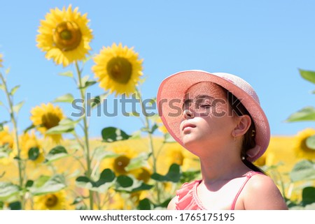 A girl with her eyes closed, wearing a pink hat, through which the sun's rays filter, generating points of light on her face, in a field of sunflowers. Concept of peace and tranquility.