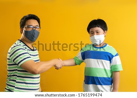 Shake hand gesture of Asian father and child, successful cooperation of generations, yellow studio background