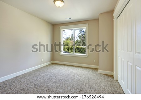 Bright empty room with one window, beige carpet floor, ivory walls and walk-in closet