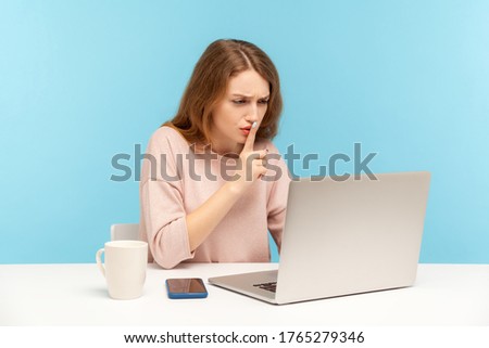 Please, keep secret. Woman employee at workplace shushing with silence gesture, talking on video call, online communication via laptop at home office. indoor studio shot isolated on blue background